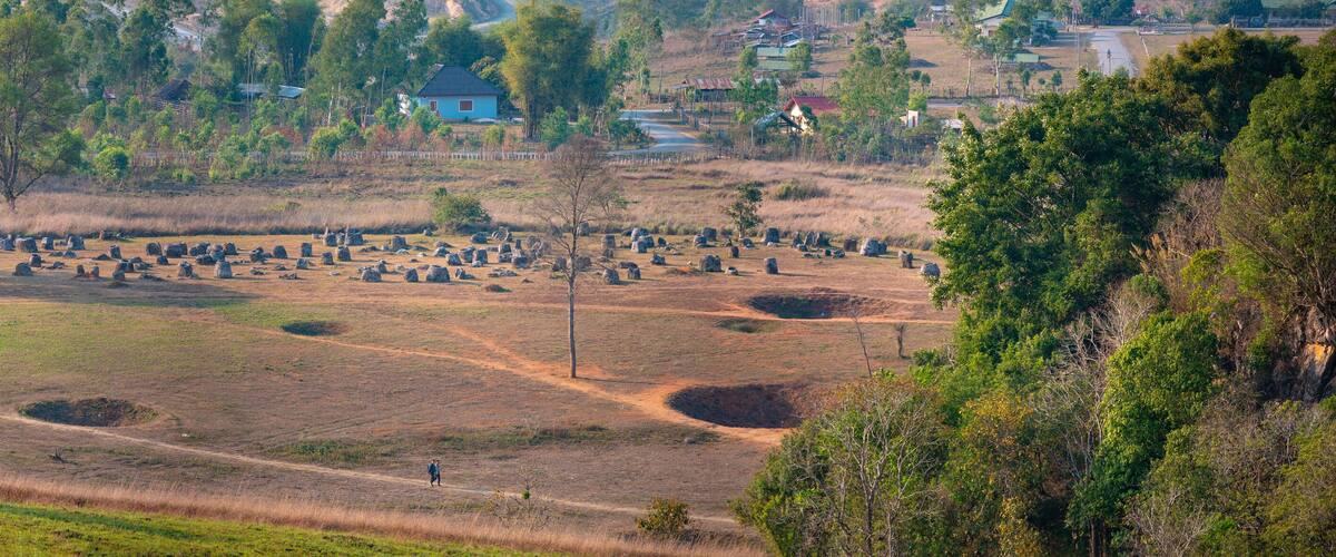 A rural landscape with scattered stone structures, a dirt path, and a blue house in the background.