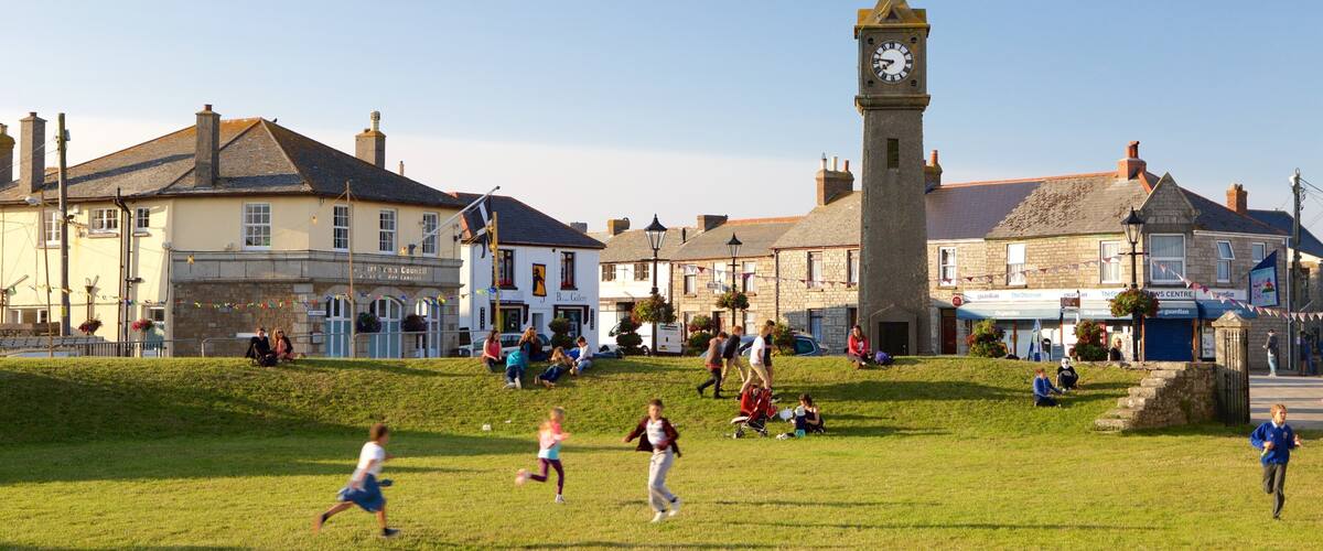 A town square with a clock tower, buildings, and people playing on the grass.
