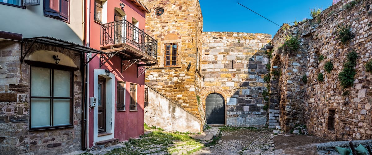 A narrow cobblestone alley flanked by historic stone buildings with arched doorways and balconies.