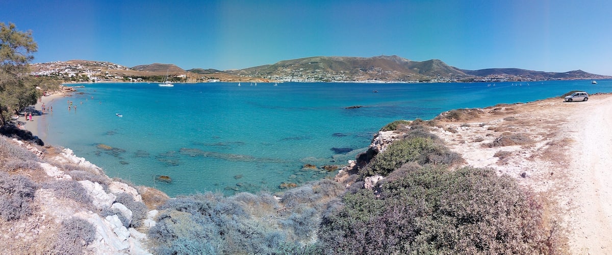A coastal landscape with clear blue waters, rocky cliffs, and a dirt path leading to a beach.