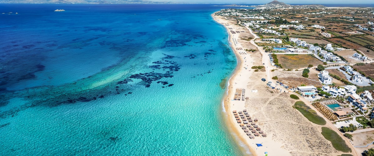 A coastal town with a beach, clear blue waters, and a mountain in the distance.