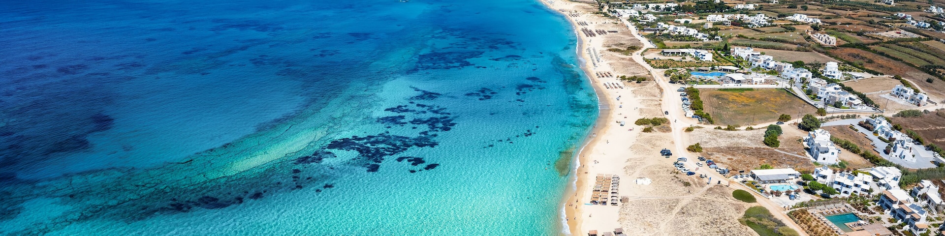 A coastal town with a beach, clear blue waters, and a mountain in the distance.
