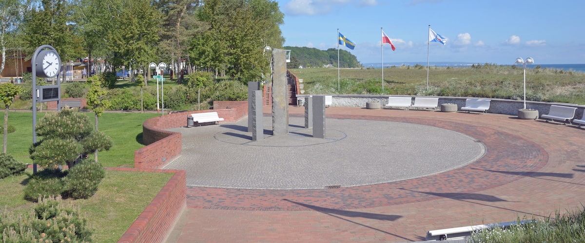A circular plaza with benches, a clock, and flags.