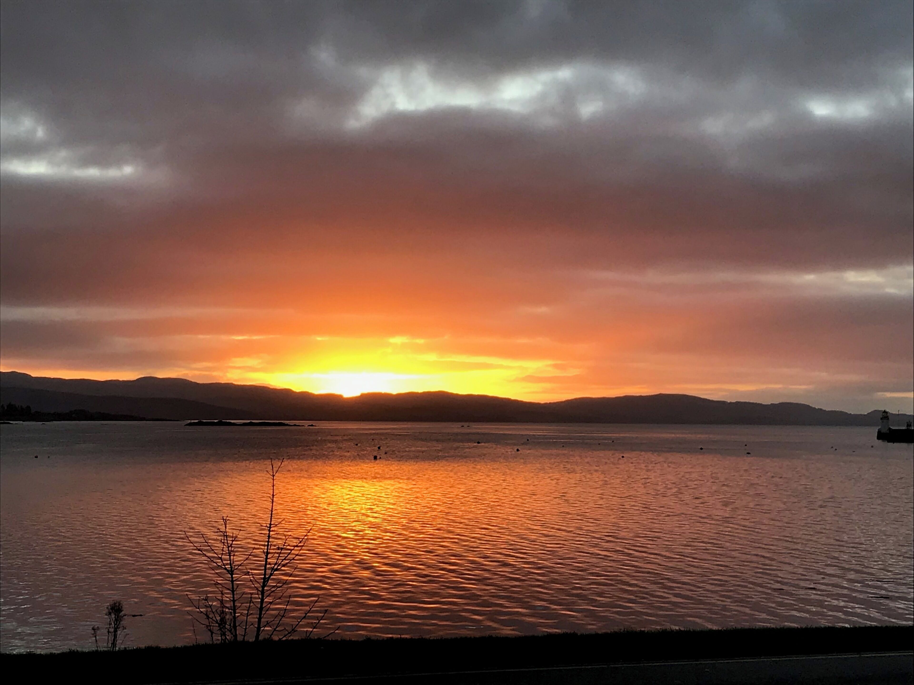 A sunset over a calm body of water with distant mountains and a lighthouse.