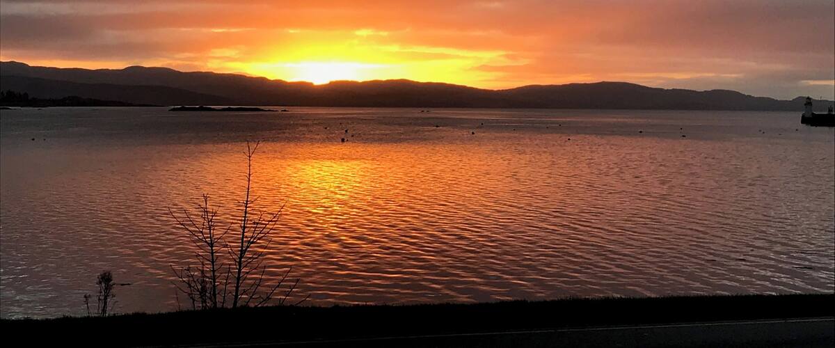 A sunset over a calm body of water with distant mountains and a lighthouse.