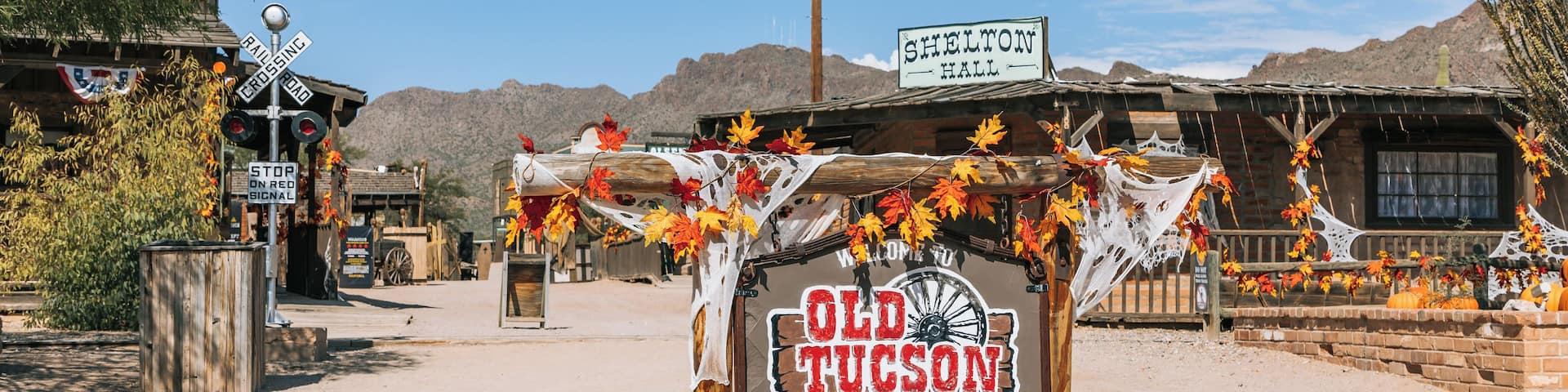 Un letrero rústico con 'Old Tucson' y temática vaquera, rodeado de paisajes desérticos y edificios de madera.