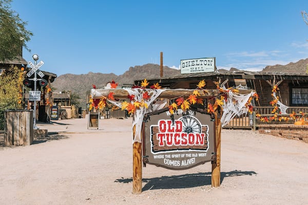 Ein rustikales Schild mit der Aufschrift 'Old Tucson' im Westernstil, umgeben von Wüstenlandschaft und Holzhäusern.