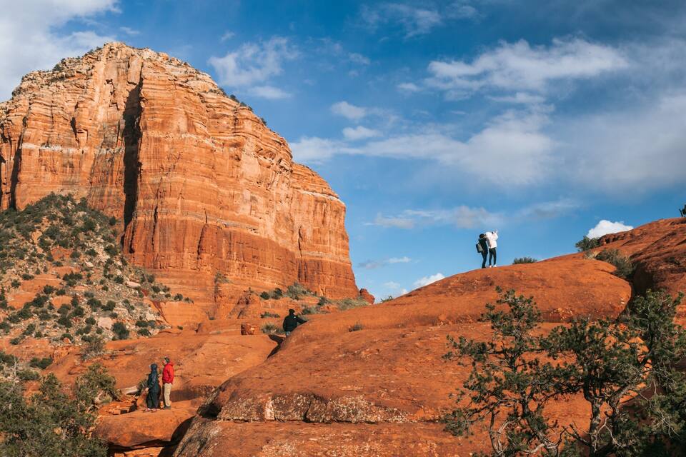 A large red rock formation with people hiking around it.