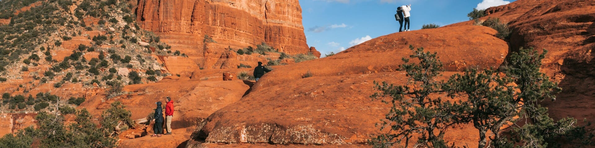 A large red rock formation with people hiking around it.