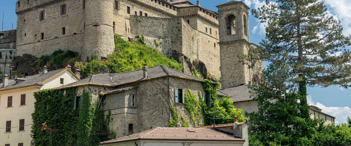 A historic stone castle with a tower, surrounded by lush greenery and traditional buildings.
