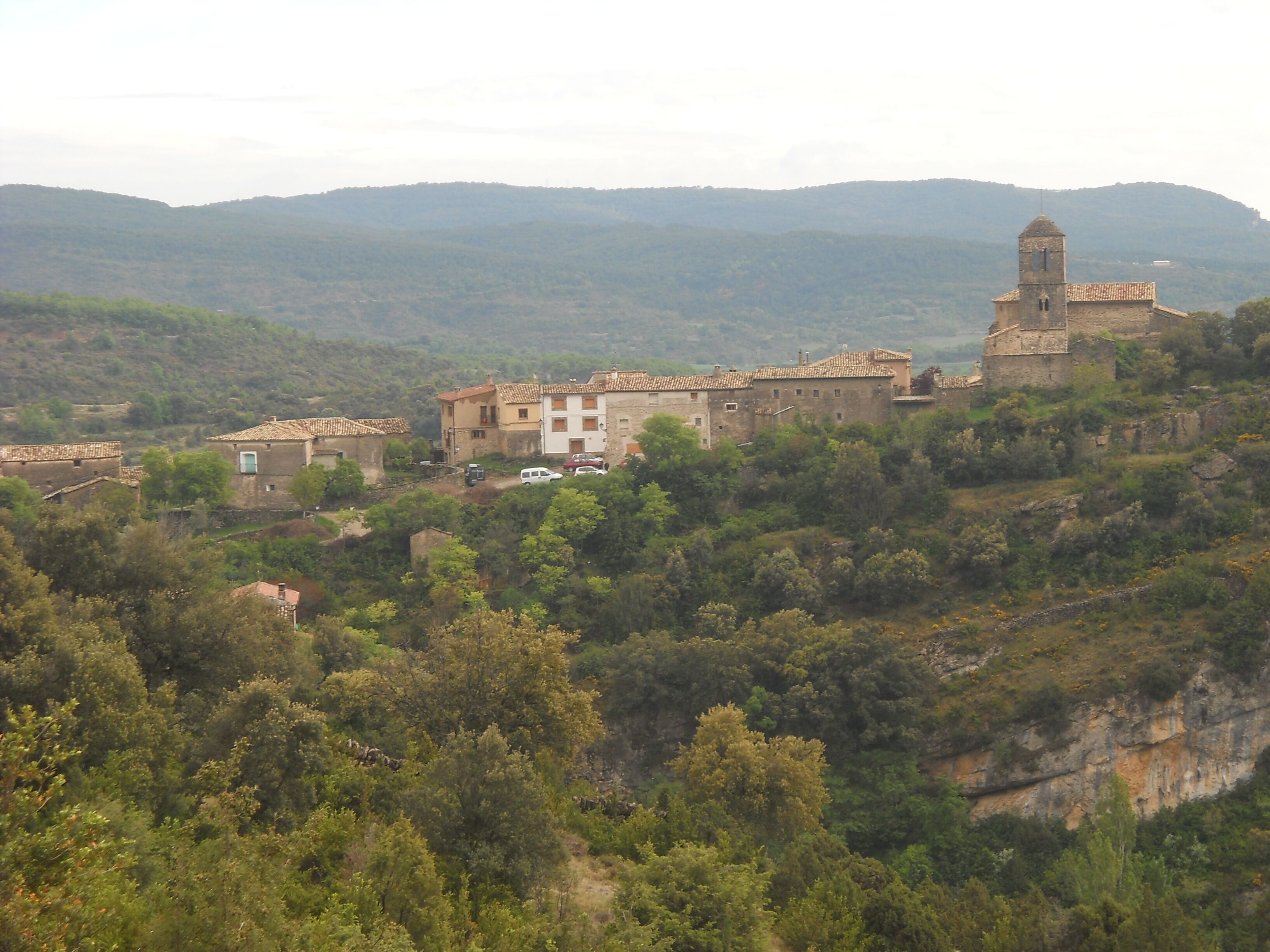 A village with stone buildings and a church on a hillside.