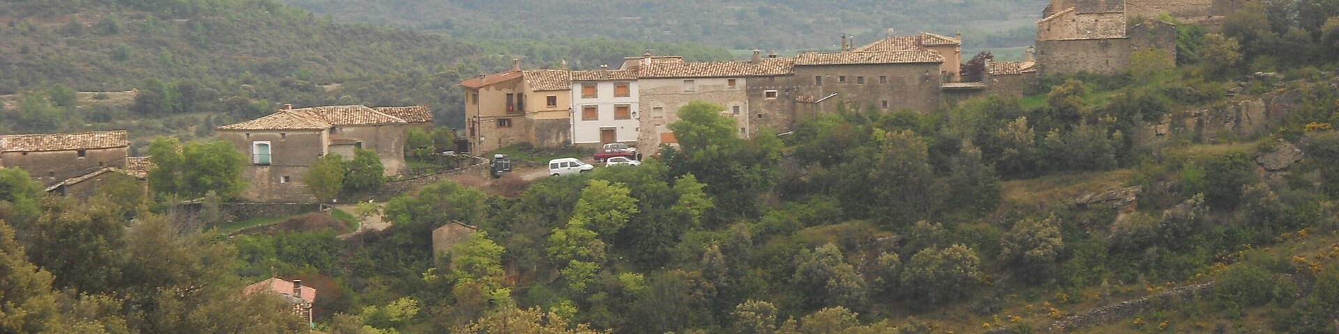 A village with stone buildings and a church on a hillside.