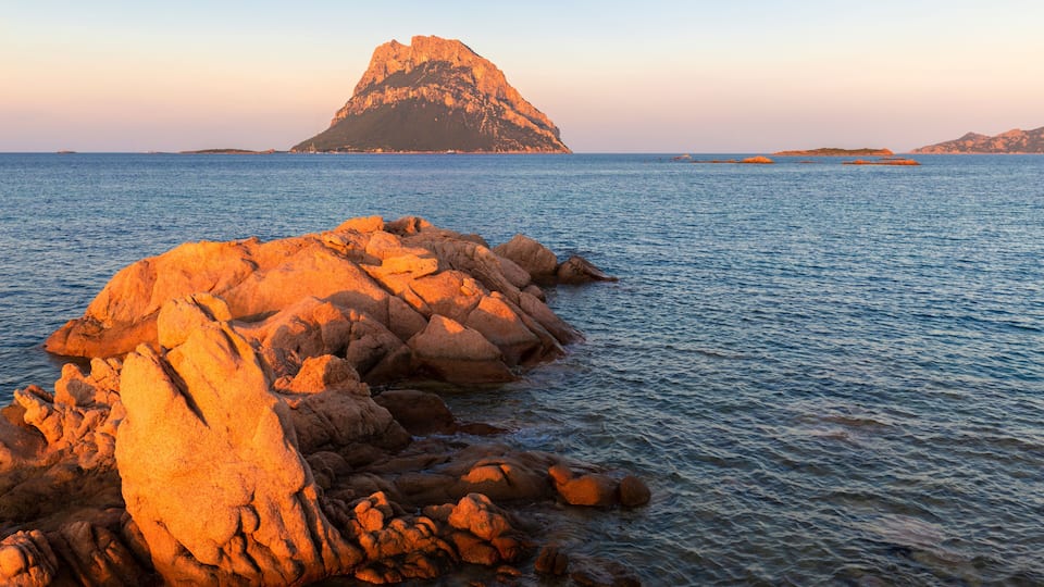A rocky coastline with a prominent hill in the distance.