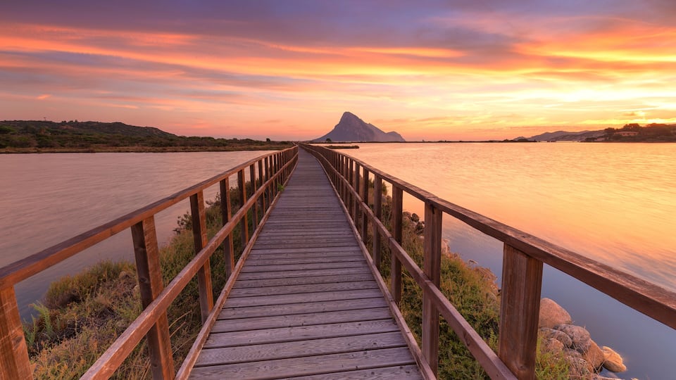 A wooden boardwalk leading to a mountain at sunset.