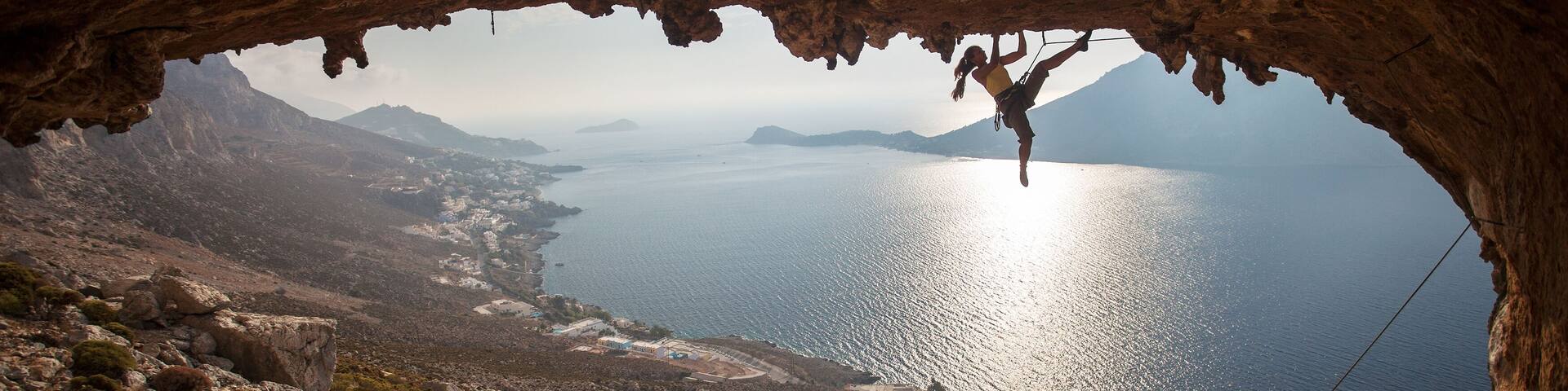 A person rock climbing inside a cave with a view of a coastal landscape.