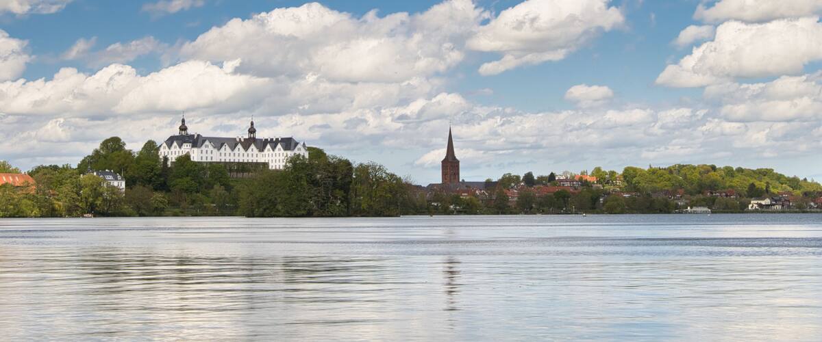 A calm lake with a white building and a church on a hill.