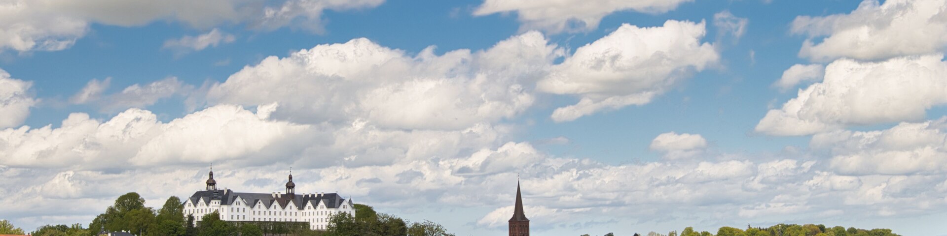 A calm lake with a white building and a church on a hill.
