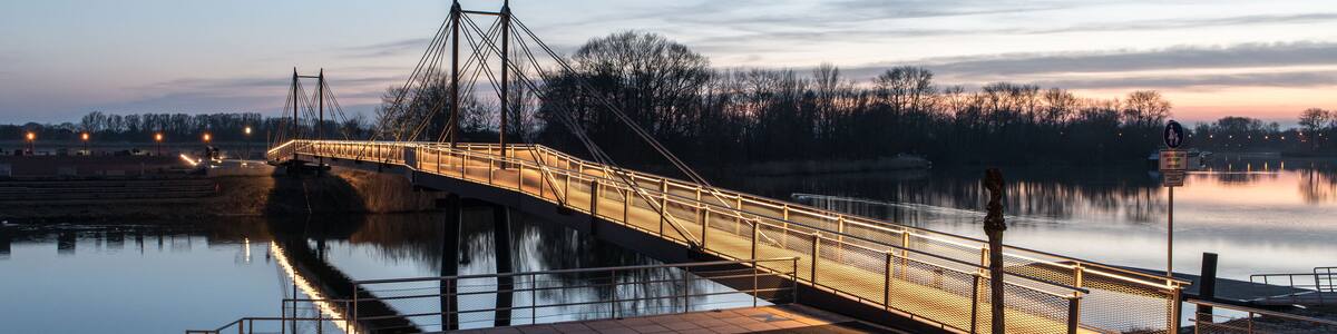 Eine Fußgängerbrücke über einem ruhigen Fluss im Dämmerlicht.