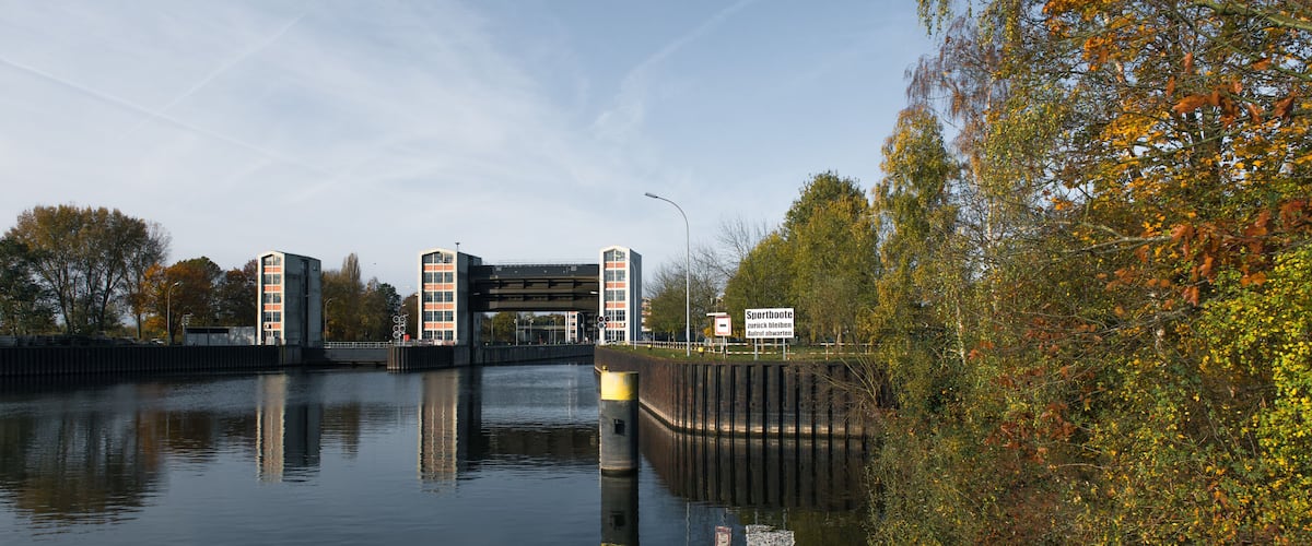 A lock with a bridge overhead, surrounded by autumn foliage and a calm river.