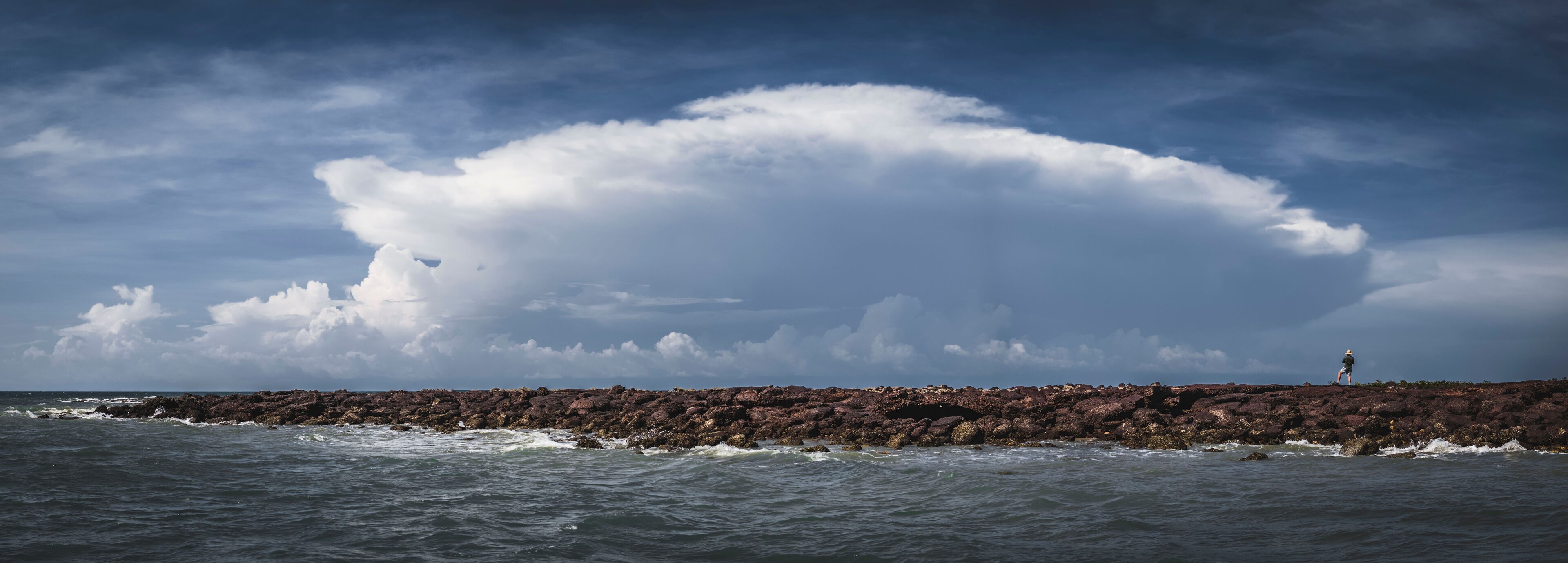A rocky coastline with waves crashing against the rocks under a cloudy sky.