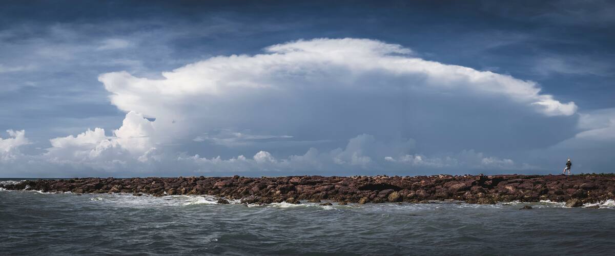 A rocky coastline with waves crashing against the rocks under a cloudy sky.