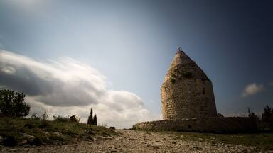 Una torre de piedra con techo cónico, rodeada por un paisaje cubierto de hierba y un cielo parcialmente nublado.