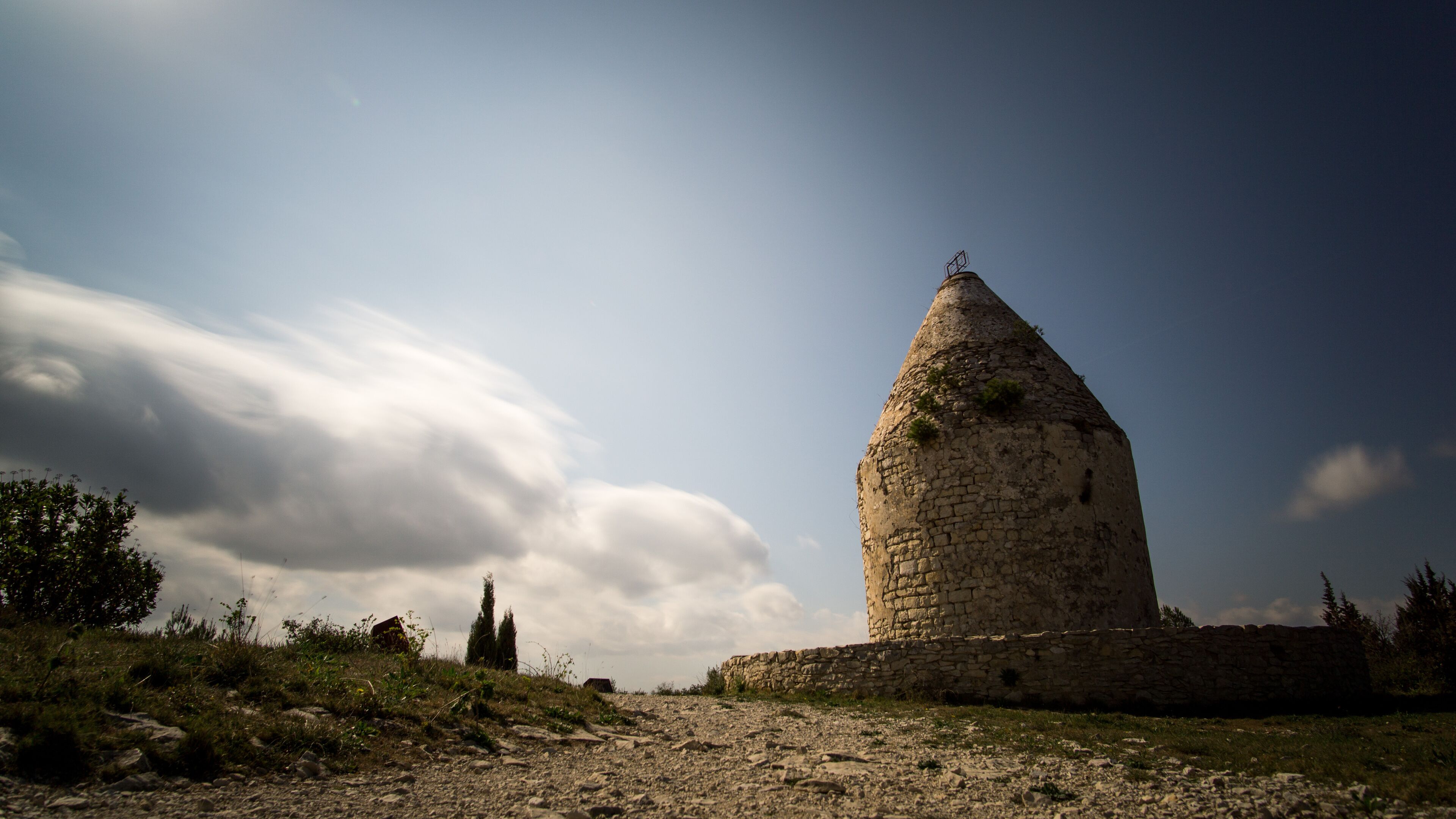 A stone tower with a conical roof, surrounded by a grassy landscape and a partly cloudy sky.