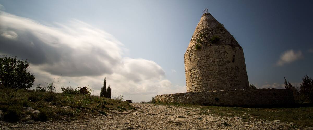 A stone tower with a conical roof, surrounded by a grassy landscape and a partly cloudy sky.