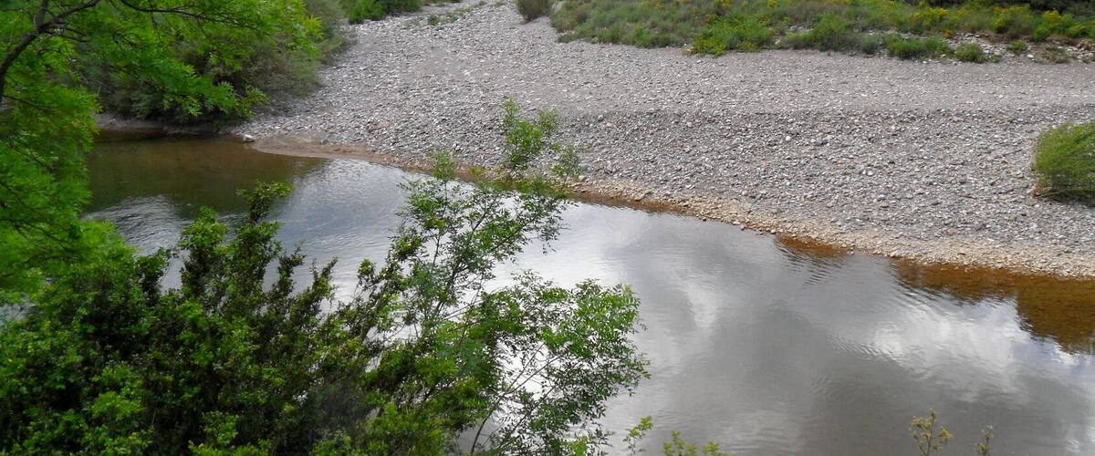 A river with a rocky bed, surrounded by dense greenery and hills.
