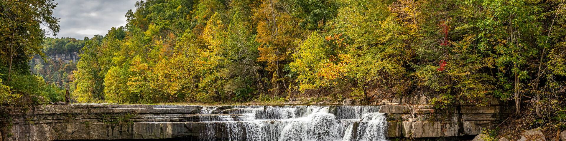 A waterfall cascading over a rocky ledge surrounded by autumn-colored trees.