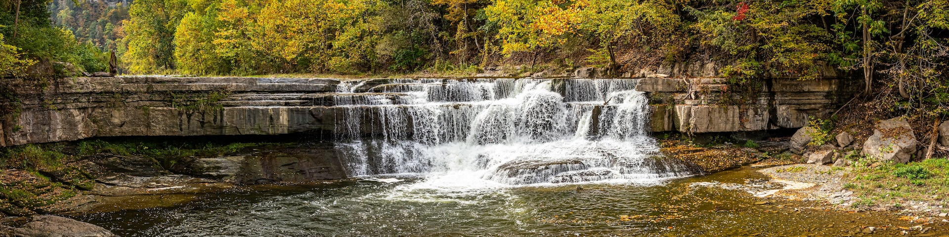 Una cascada se precipita sobre un saliente rocoso rodeado de árboles de colores otoñales.