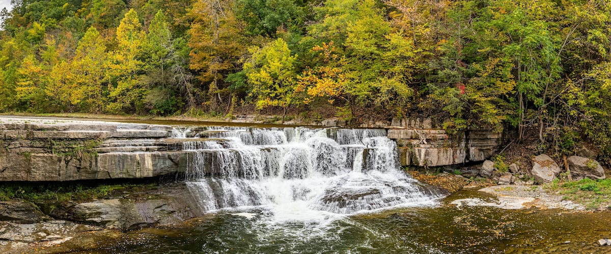 A waterfall cascading over a rocky ledge surrounded by autumn-colored trees.