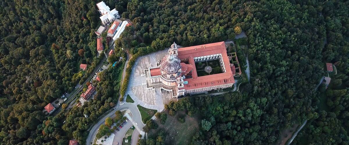 An aerial view of a historic building with a dome, surrounded by dense forest and a winding road.