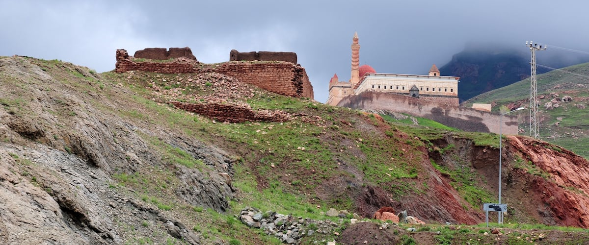 Ancient ruins on a hillside, a mosque with a minaret, and a modern building in the background.