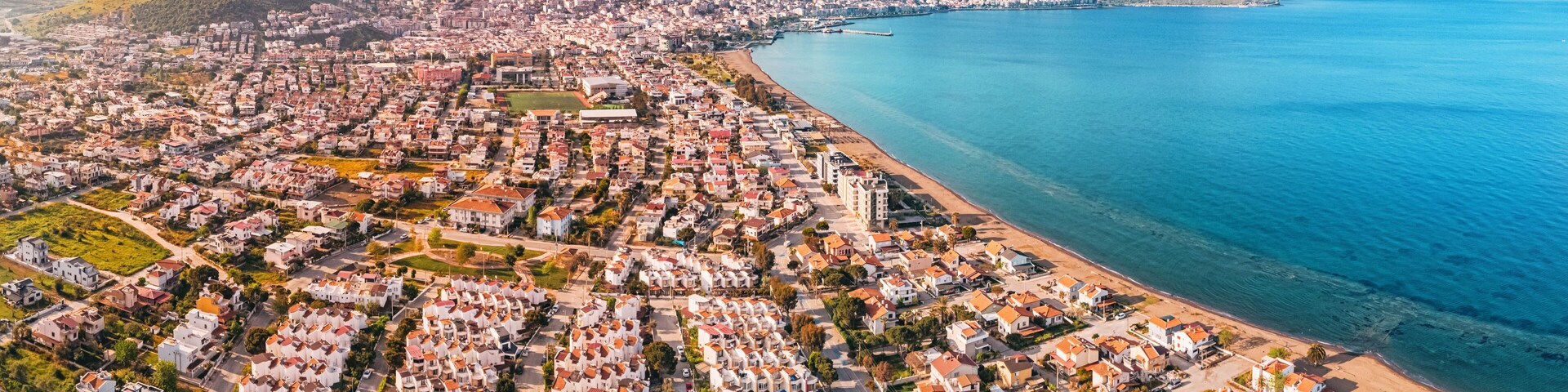 Drone capturing the cityscape of Dikili, its residential neighborhoods, the Aegean Sea, and the surrounding mountains in Turkiye