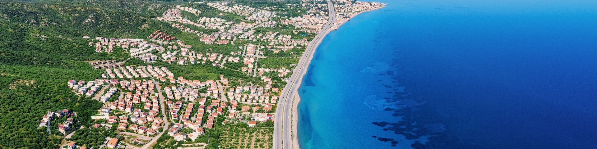 Vista aérea de un pueblo costero con playa, zonas residenciales y colinas circundantes.