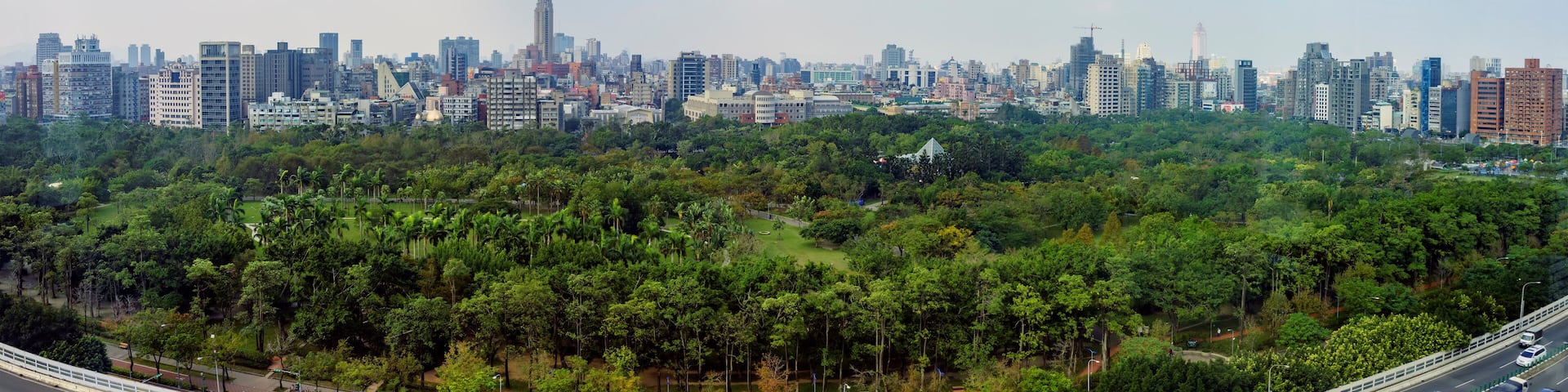 A city skyline with dense urban buildings and a lush green park in the foreground.