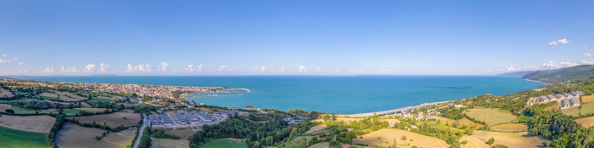 A coastal landscape with fields, a road, and a distant city by the sea.