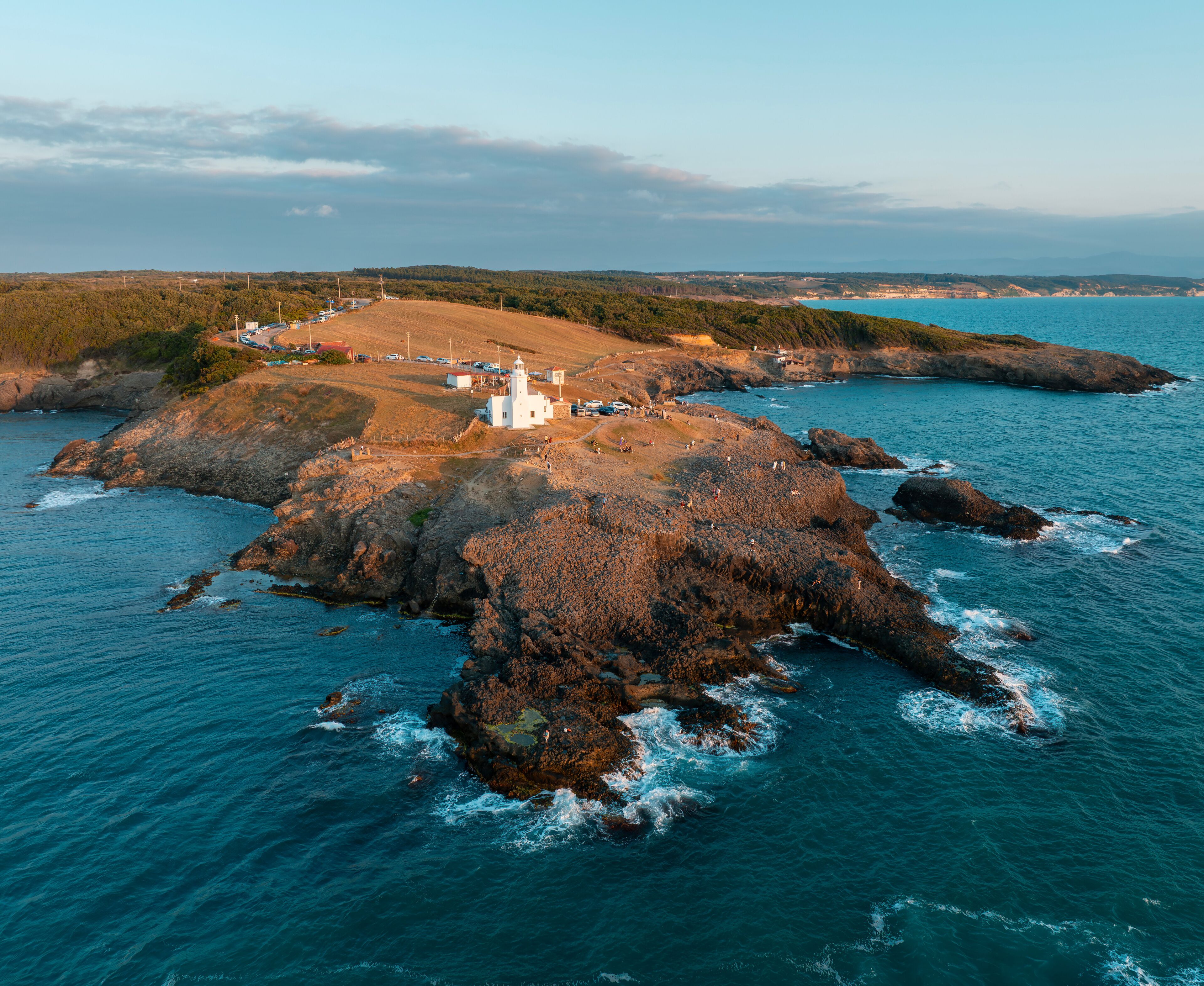 Un paisaje costero con un faro, afloramientos rocosos y una costa lejana.