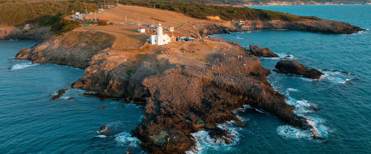 A coastal landscape with a lighthouse, rocky outcrops, and a distant shoreline.