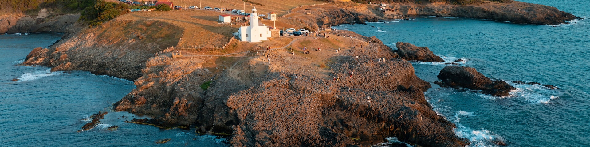 Un paisaje costero con un faro, afloramientos rocosos y una costa lejana.