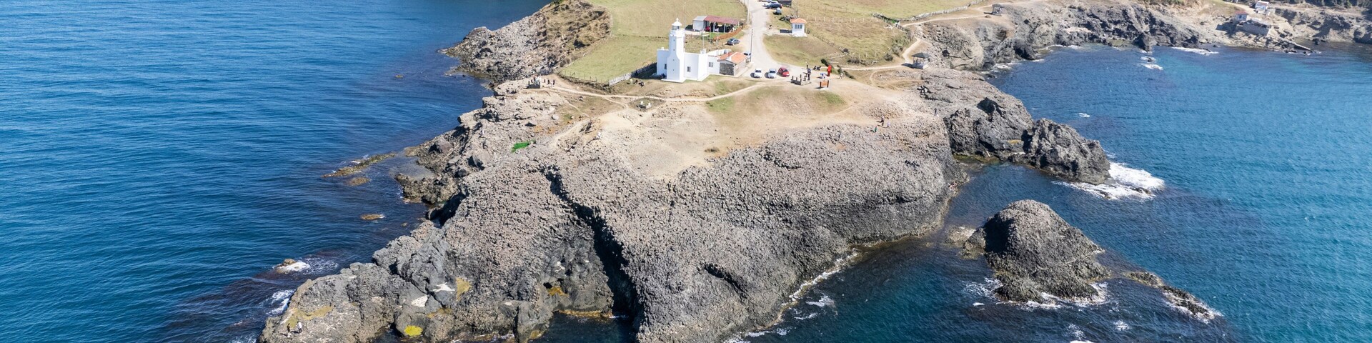 Un faro costero sobre un promontorio rocoso con una vista despejada del paisaje circundante y el océano.