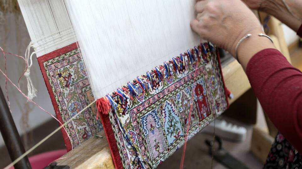 A person weaving a colorful textile with intricate patterns.