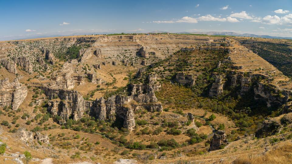 A rugged canyon landscape with rocky formations and sparse vegetation.