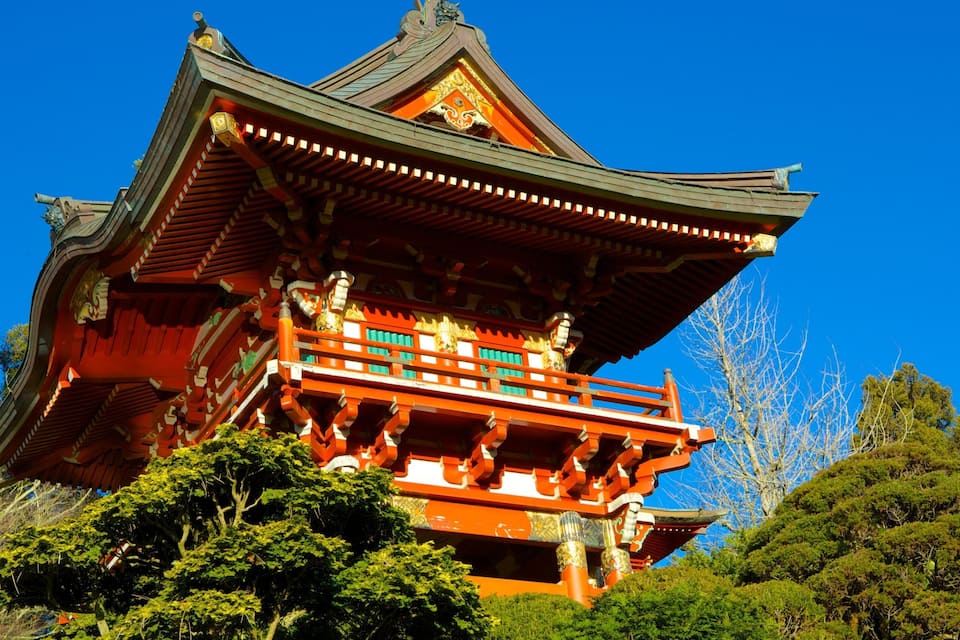 A traditional Japanese pagoda with a red and gold roof, surrounded by lush greenery.