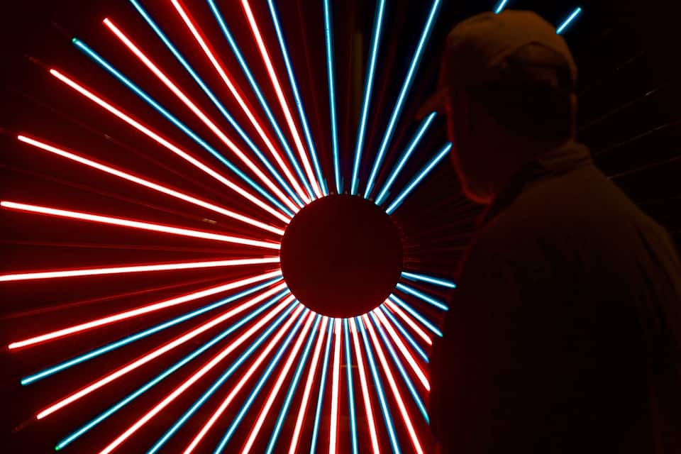A person standing in front of a circular light installation with red and blue lights radiating outward.