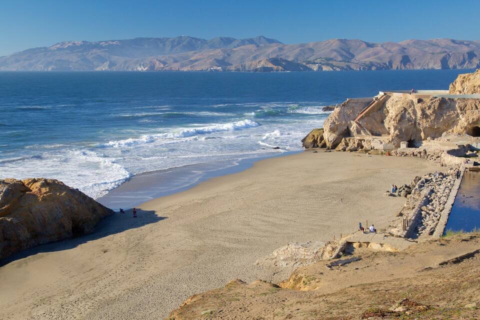 A coastal landscape with a sandy beach, rocky cliffs, and a clear blue ocean.