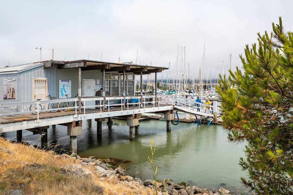 Un muelle se adentra en aguas tranquilas, con un edificio a la izquierda y barcos amarrados cerca.