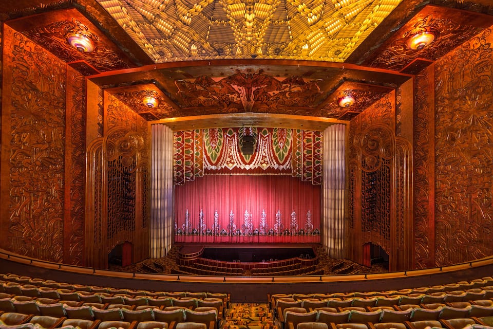 An ornate theater with intricate carvings and a red curtain.