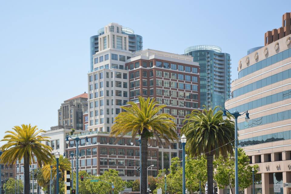 A cityscape with modern buildings, palm trees, and street lamps.